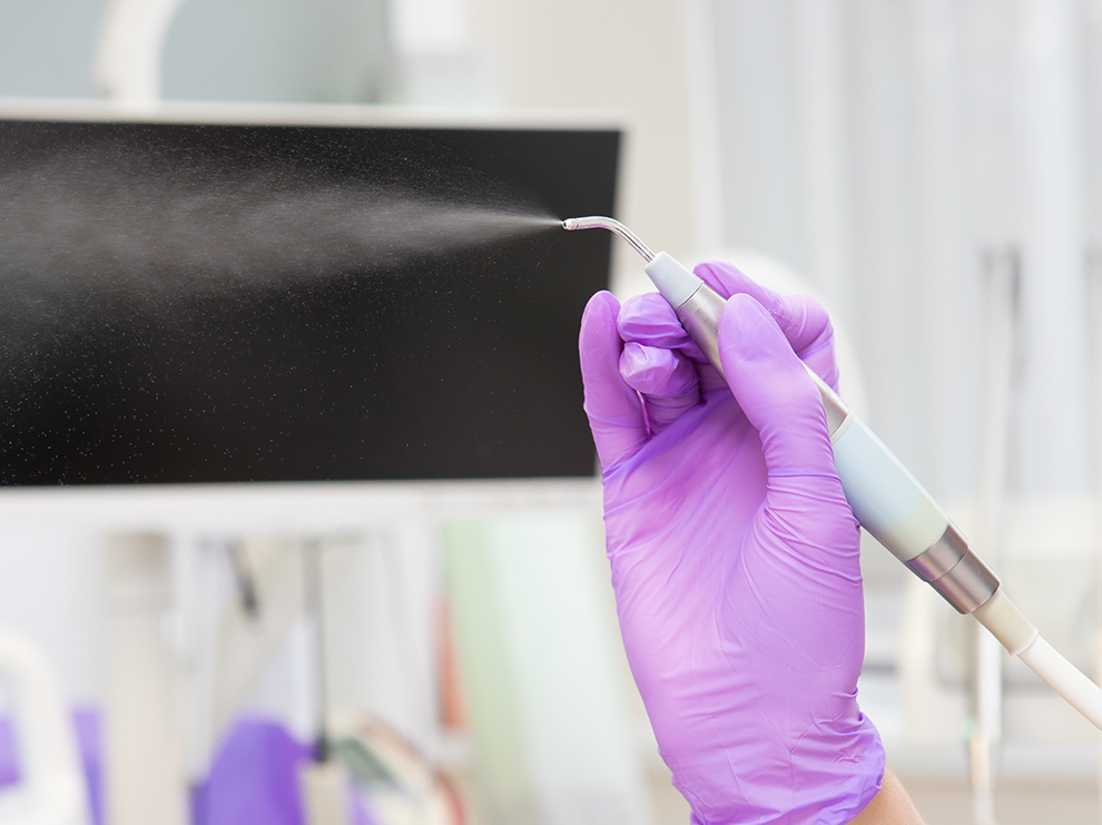 dental hygienist holding up Air-Flow machine and spraying water jet