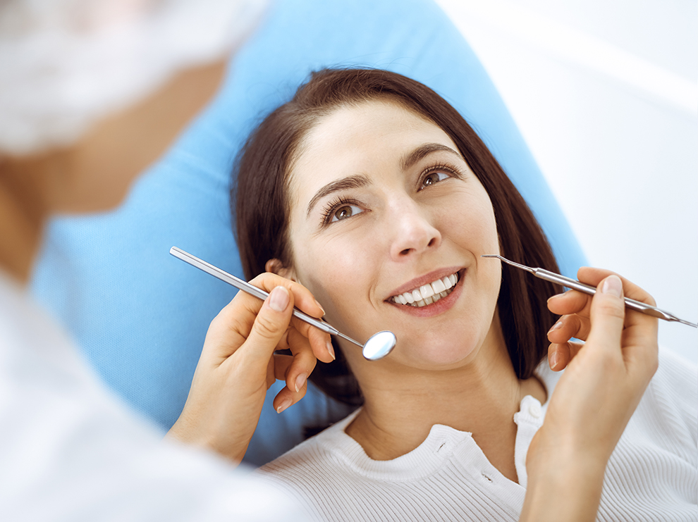 Dental hygienist in Leigh on Sea holding mouth mirror and explorer tool above smiling patient mouth